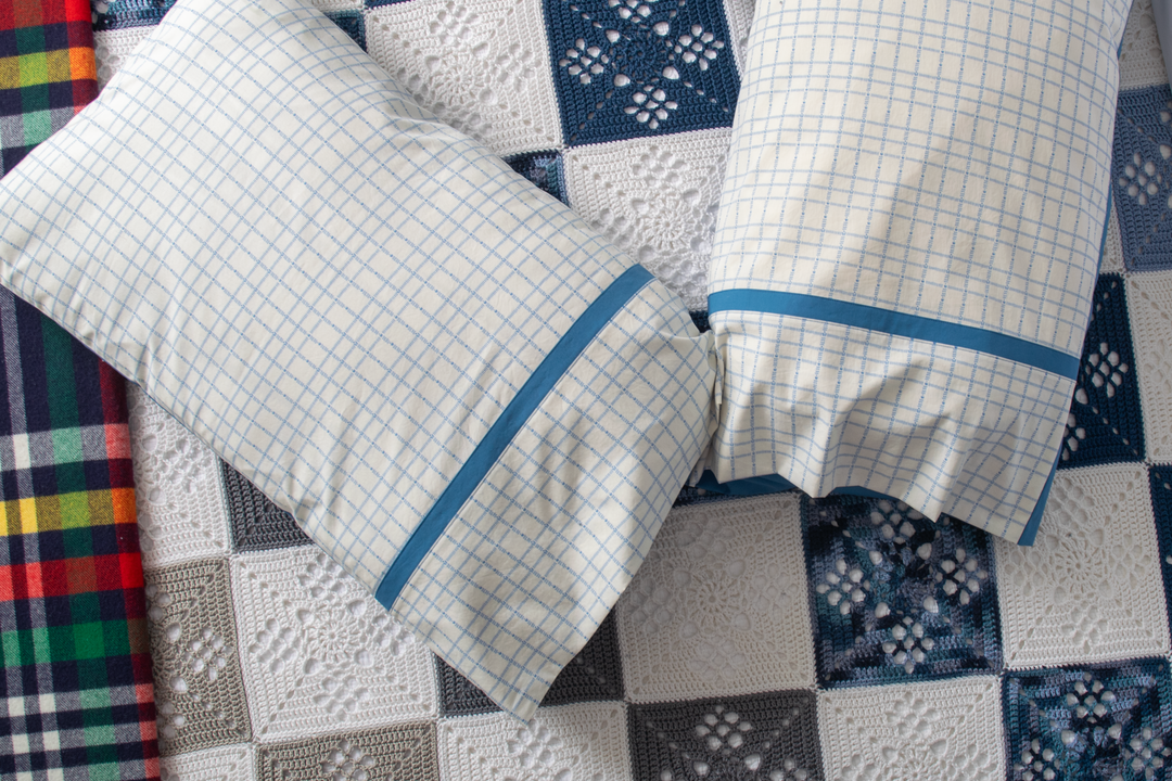 Checkered pillowcases with blue trim on a crocheted blanket background