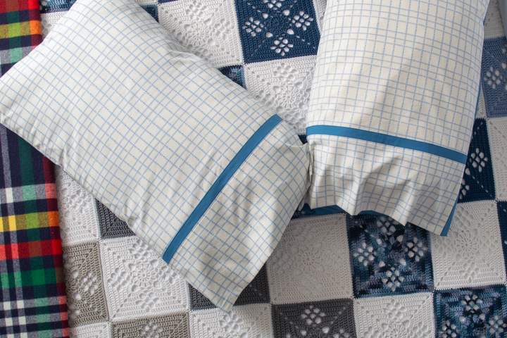 Checkered pillowcases with blue trim on a crocheted blanket background